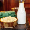 A wooden bowl filled with soybeans a tall glass container of soy milk.