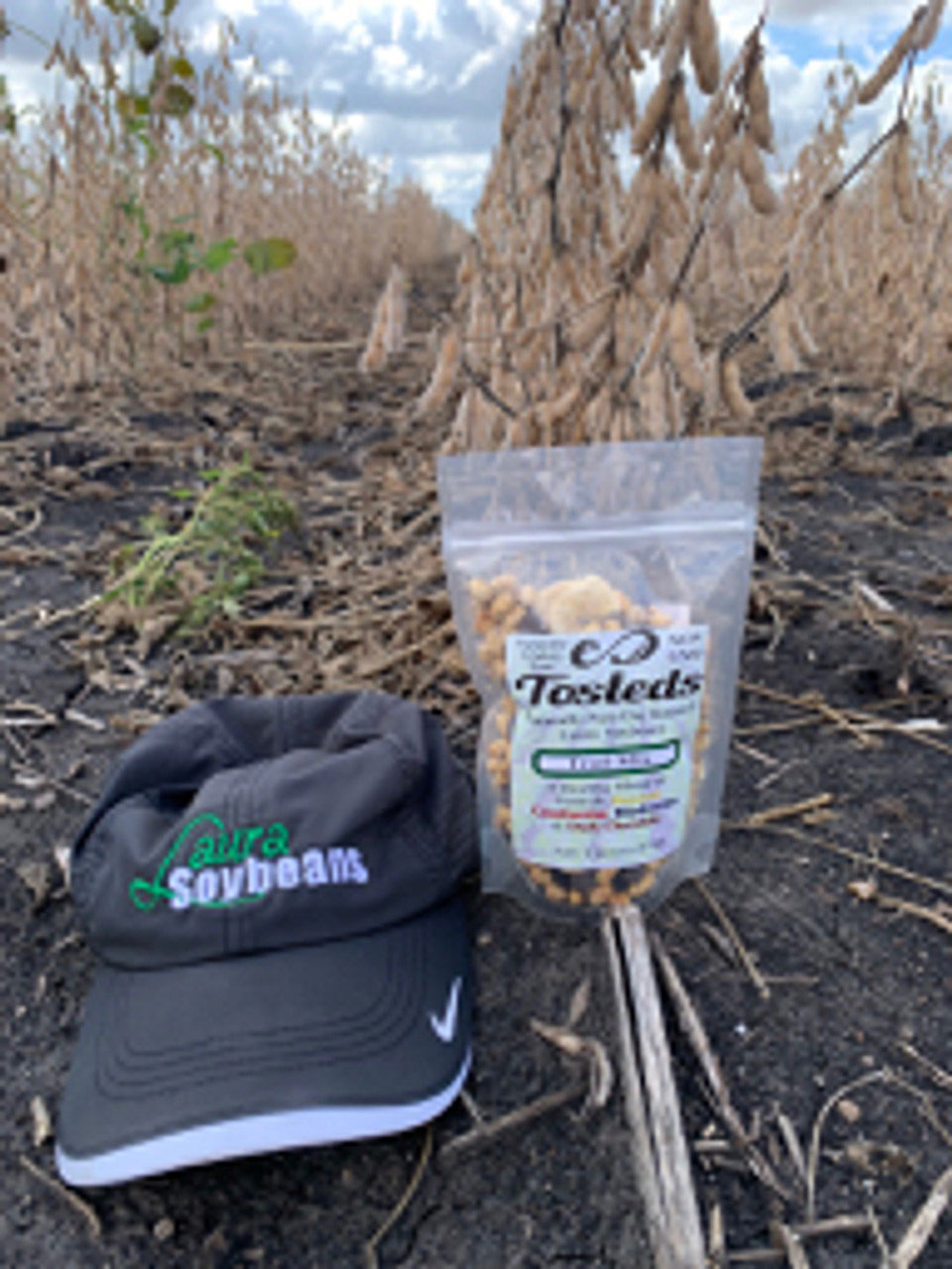 A Laura Soybeans hat next to a resealable bag of Tosteds Trail Mix, sitting in the Laura Soybeans field.