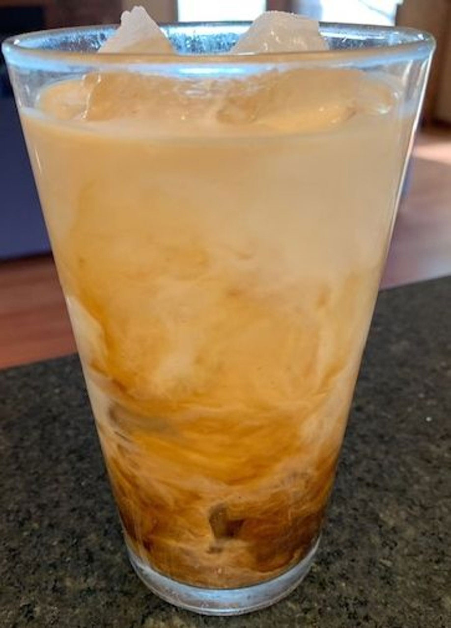A tall glass of iced Laura Soy Coffee with creamer mixing in.