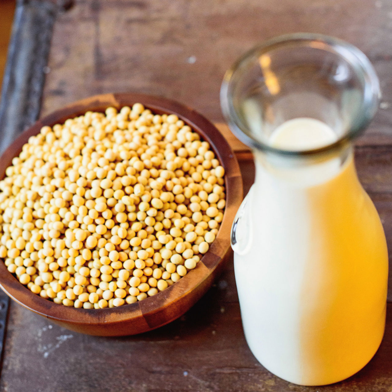 A wooden bowl filled with soybeans a tall glass container of soy milk.