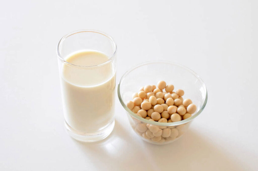 A glass of soymilk next to a small glass bowl filled with soybeans.