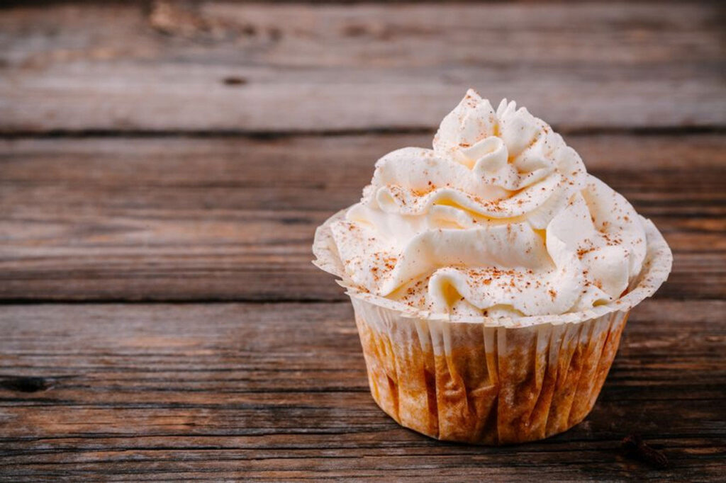 A closeup of a vegan cupcake with white frosting and cinnamon sprinkled on top.