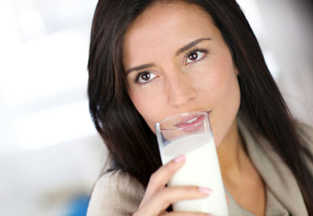 A woman taking a drink from a glass of soymilk.