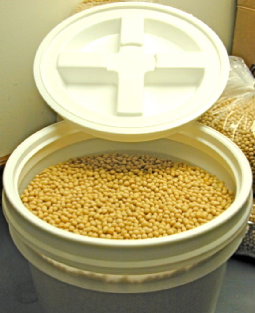 A large, white tub with the lid offset, filled to the top with Laura Soybeans.