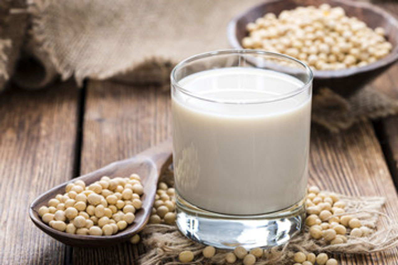 A glass of soymilk with soybeans placed artfully around it.