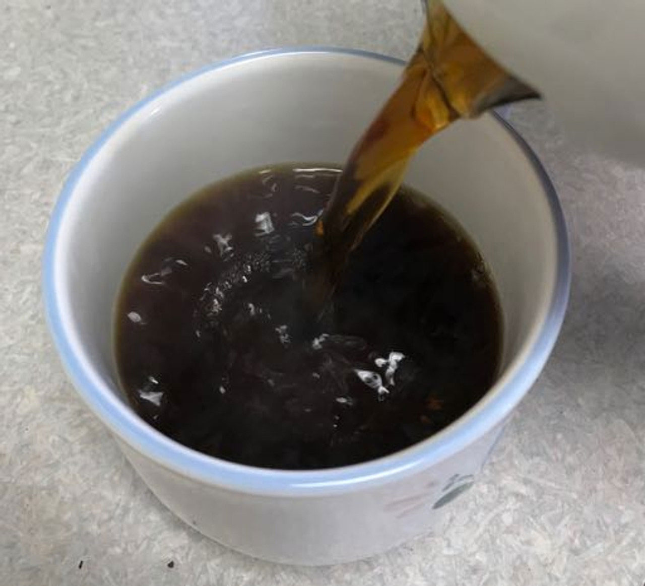 A close up of a pitcher pouring hot Laura Soybean coffee into a white teacup.
