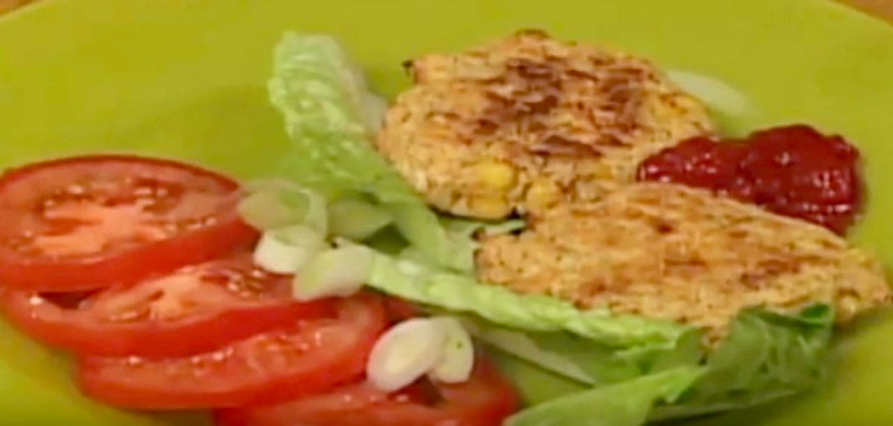 A green plate with slices of tomatoes, lettuce, Okara burgers, and some ketchup.