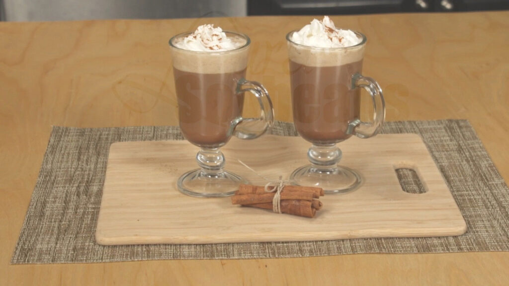 Two glass mugs filled with soy coffee mocha lattes, topped with whipped cream a dusting of cinnamon.