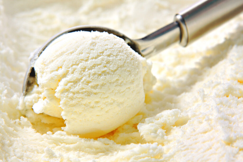 A close up of a metal ice cream scoop scooping up vanilla soy milk ice cream