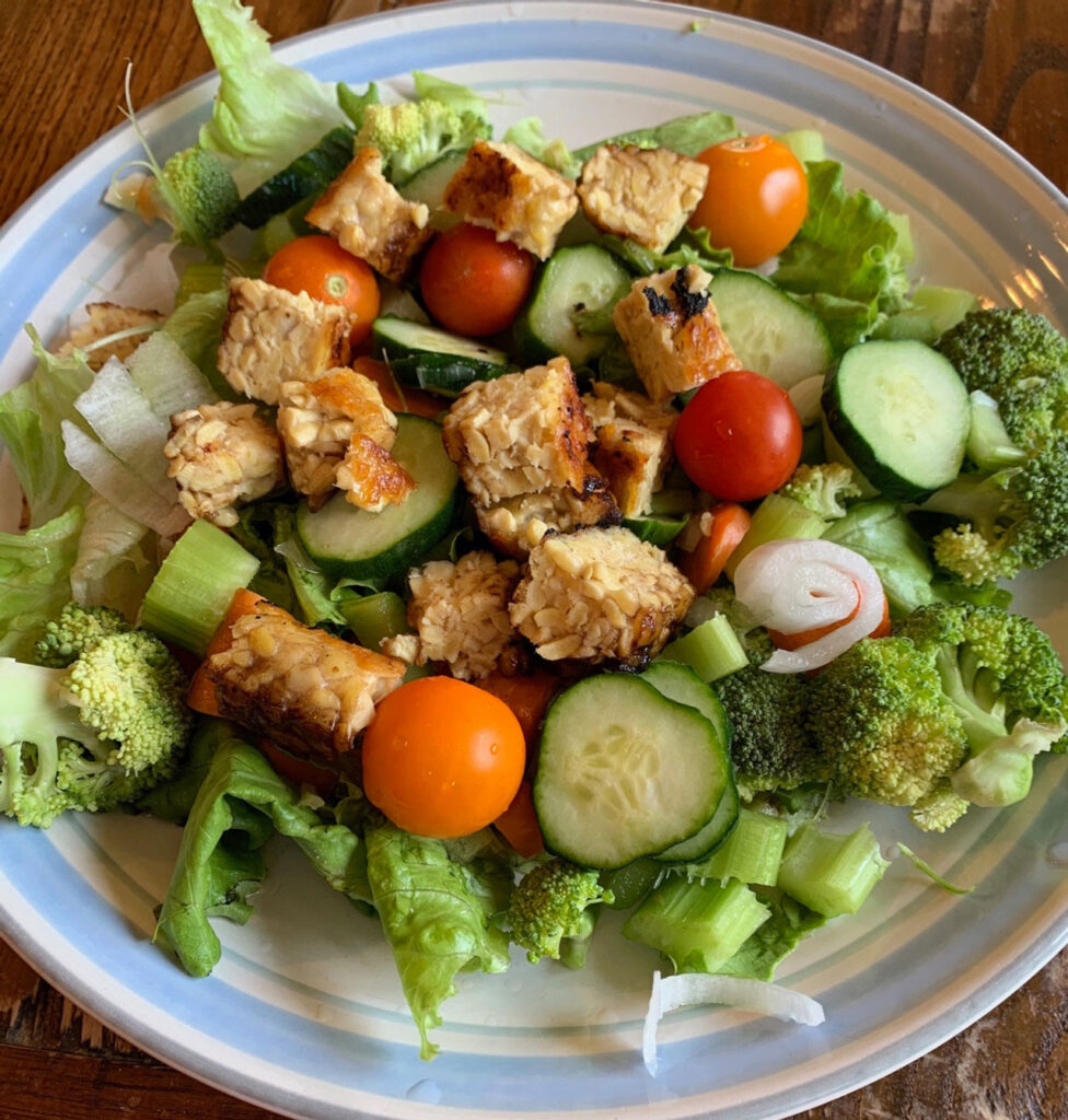 A salad with lettuce, broccoli, red and orange cherry tomatoes, celery, and tempeh.
